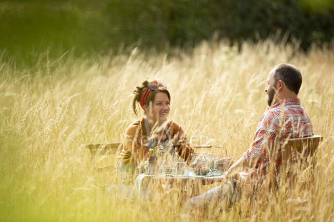Glückliches Paar entspannt sich am Tisch im sonnigen hohen Gras — Stockfoto
