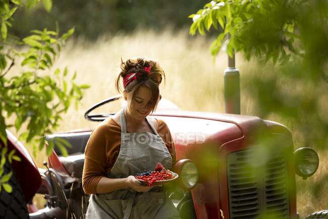 Happy woman with fresh harvested red currants at tractor — Stock Photo