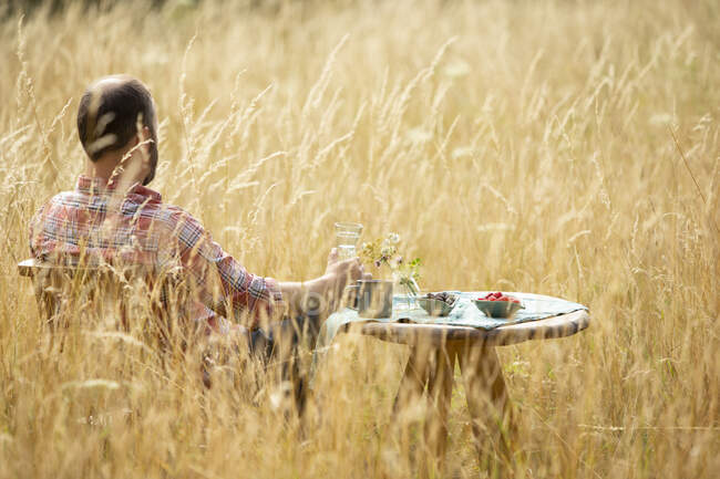 Homme relaxant à table dans l'herbe haute ensoleillée d'été — Photo de stock