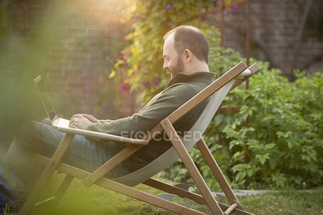 Man working at laptop in lawn chair in summer garden — Stock Photo