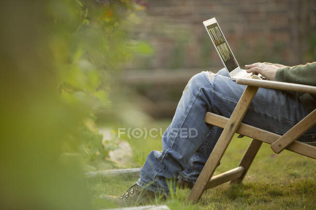 Mann benutzt Laptop im Rasenstuhl im Garten — Stockfoto