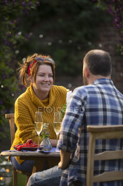 Joyeux couple dégustant champagne et groseilles rouges à table de jardin — Photo de stock