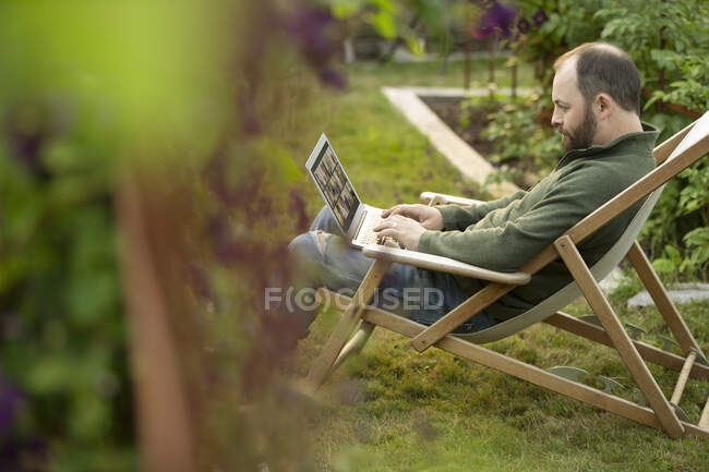 Man working at laptop in lawn chair in summer garden — Stock Photo