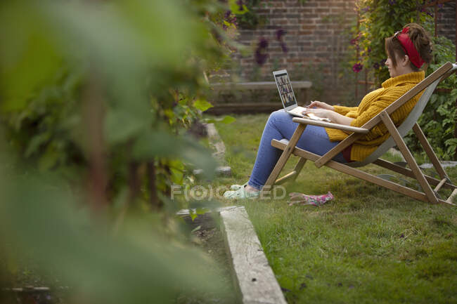 Woman working at laptop in lawn chair in summer garden — Stock Photo