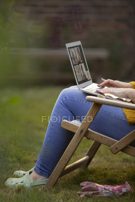 Mujer usando el ordenador portátil en silla de jardín césped - foto de stock