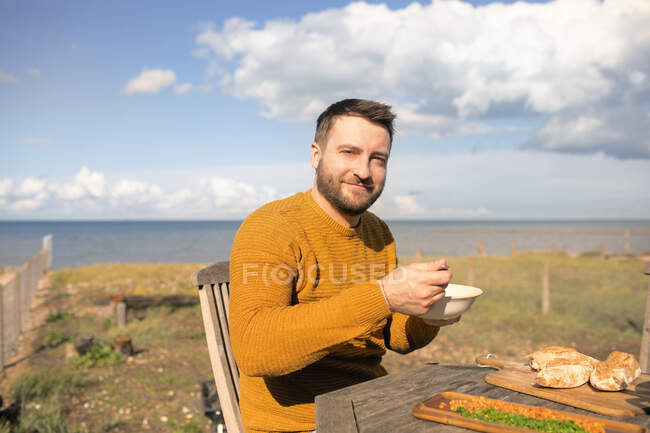 Retrato feliz hombre comiendo en soleado océano playa patio - foto de stock