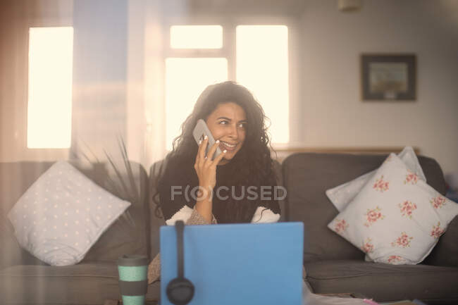 Sorrindo mulher trabalhando em casa falando no telefone inteligente no laptop — Fotografia de Stock