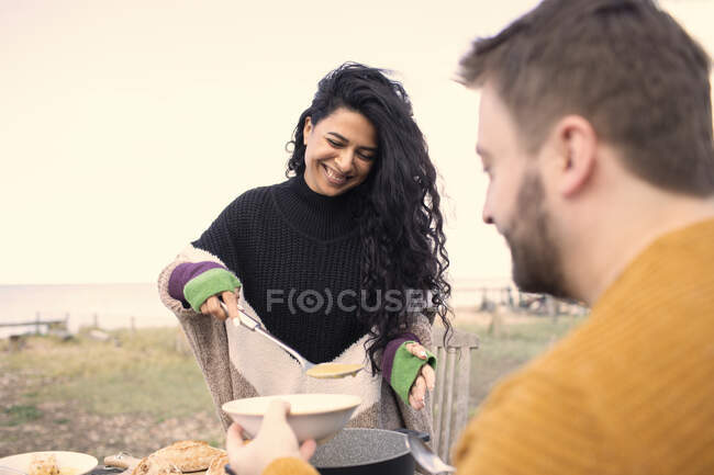 Happy woman serving chowder to boyfriend on beach patio — Stock Photo