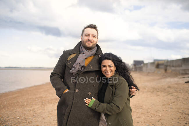 Портрет щаслива ласкава пара в зимових пальто обіймається на пляжі — стокове фото