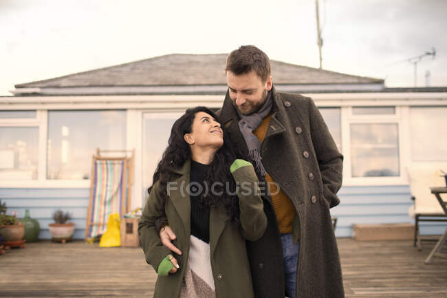 Happy couple in winter coats hugging outside house — Stock Photo