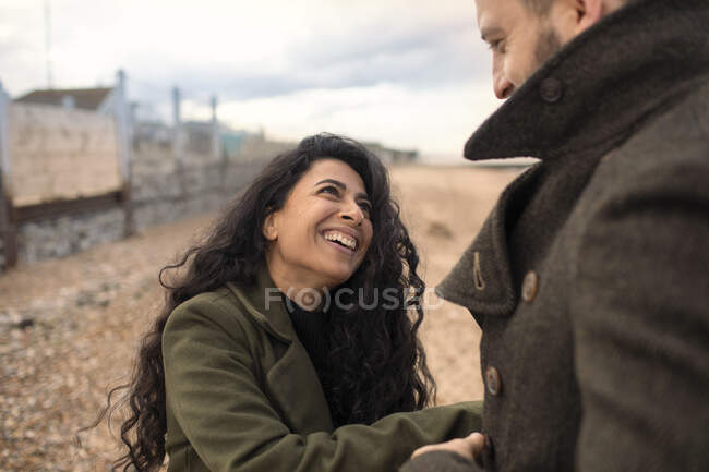 Glückliches verspieltes Paar in Wintermänteln am Strand — Stockfoto