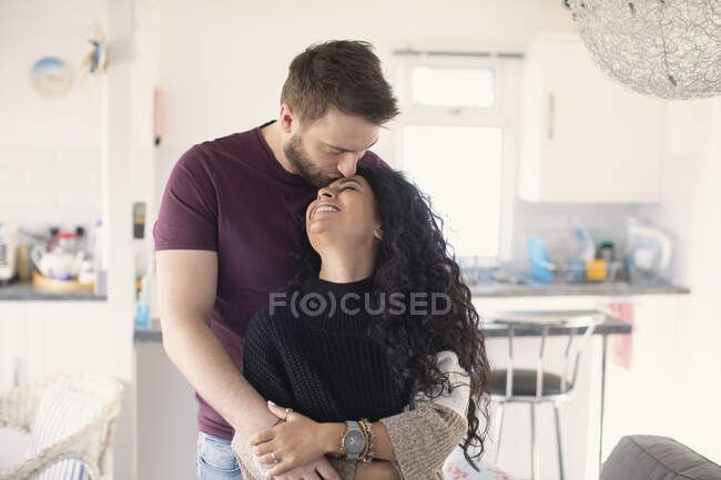 Feliz casal afetuoso abraçando e beijando na cozinha — Fotografia de Stock