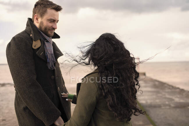 Affectionate couple in winter coats on beach jetty — Stock Photo