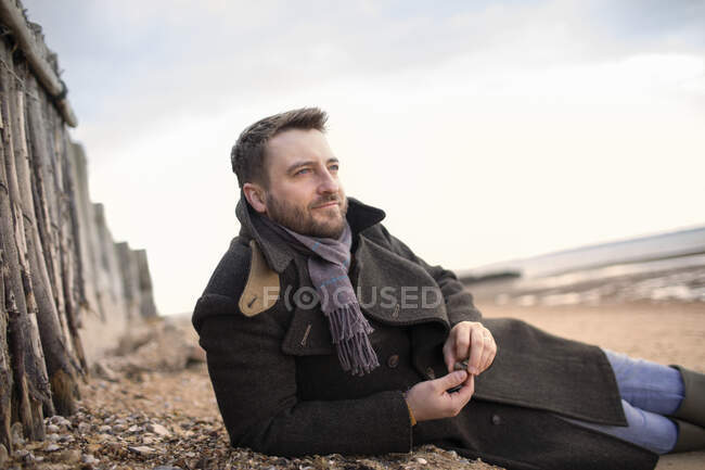 Serene man in winter coat relaxing on beach — Stock Photo