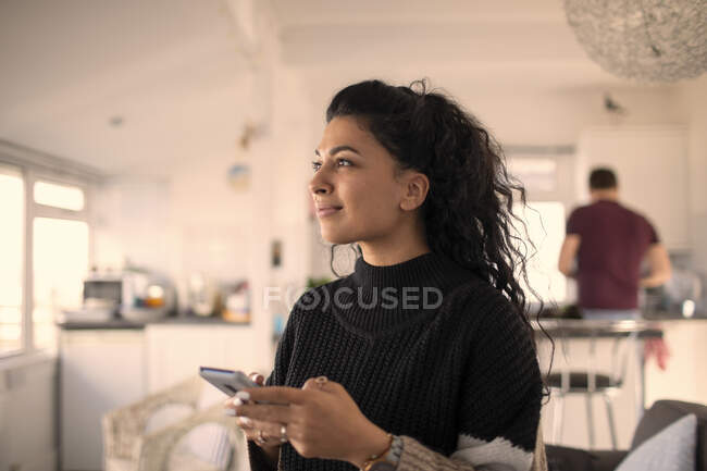 Усміхнена красива жінка використовує смартфон вдома — стокове фото