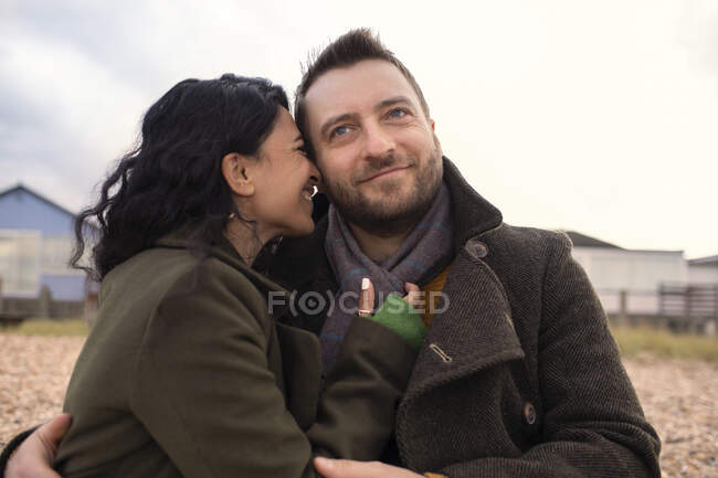 Счастливая любящая пара в зимних пальто, обнимающая на пляже — стоковое фото