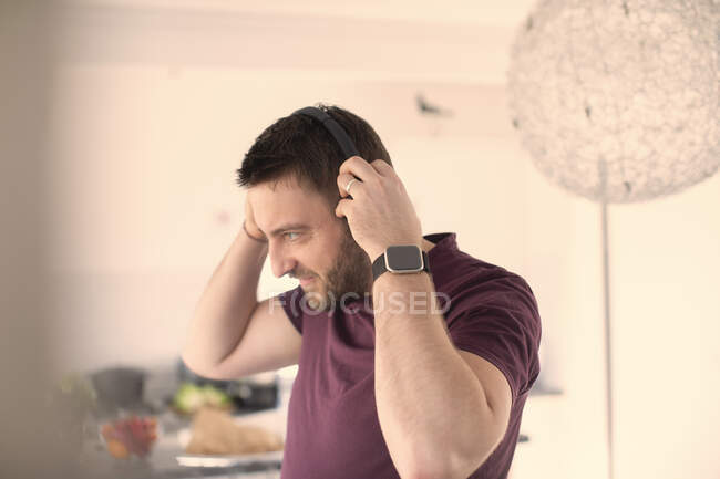 Uomo con orologio intelligente e cuffie che ascolta musica a casa — Foto stock