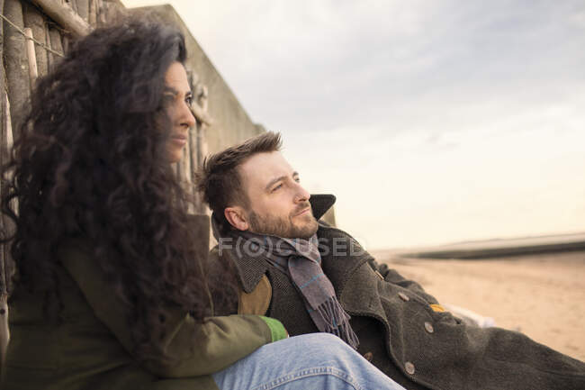 Serene couple in winter coat relaxing on beach — Stock Photo