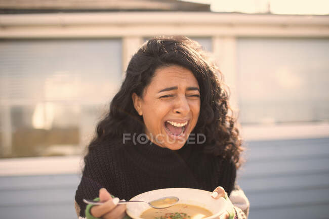 Heureuse femme rieuse mangeant de la chaudrée sur un patio ensoleillé — Photo de stock