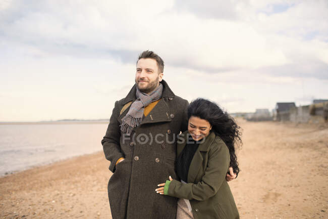 Pareja feliz en abrigos de invierno caminando en la playa del océano - foto de stock