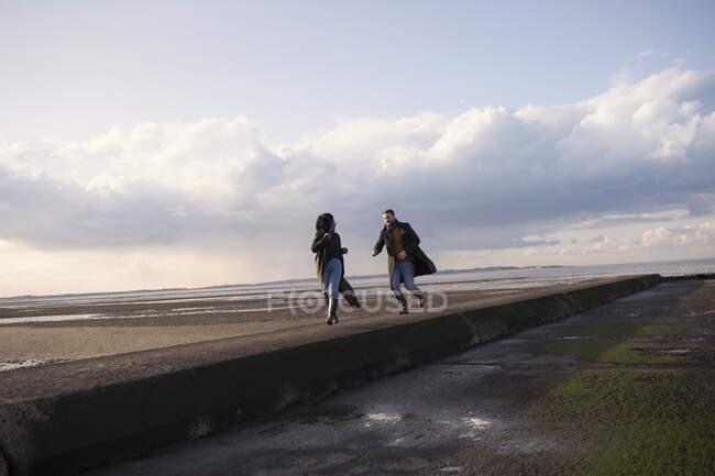 Couple running on ocean beach jetty — Stock Photo