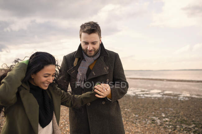 Happy couple in winter coats holding hands walking on beach — Stock Photo