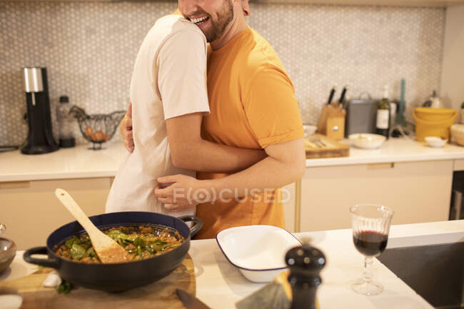 Feliz gay macho pareja cocinar y abrazos en cocina - foto de stock