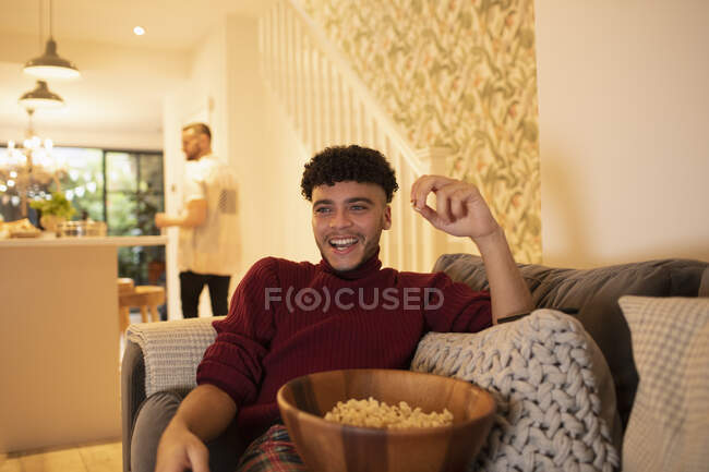 Happy young man with popcorn watching TV on living room sofa — Stock Photo