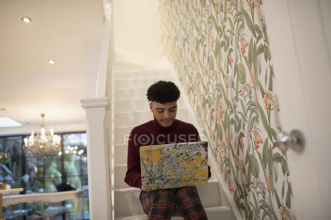 Young man using laptop on apartment stairs — Stock Photo