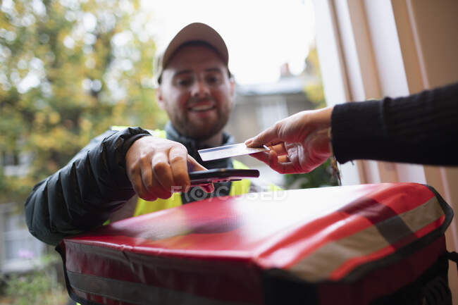 Cliente pagando homem de entrega com cartão sem contato na porta da frente — Fotografia de Stock