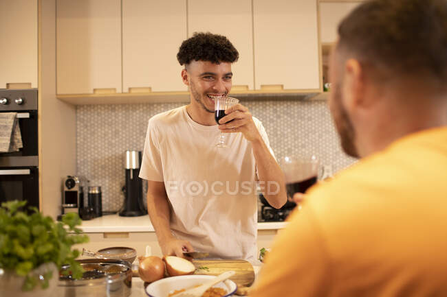 Feliz gay macho pareja bebiendo vino y cocina en cocina - foto de stock