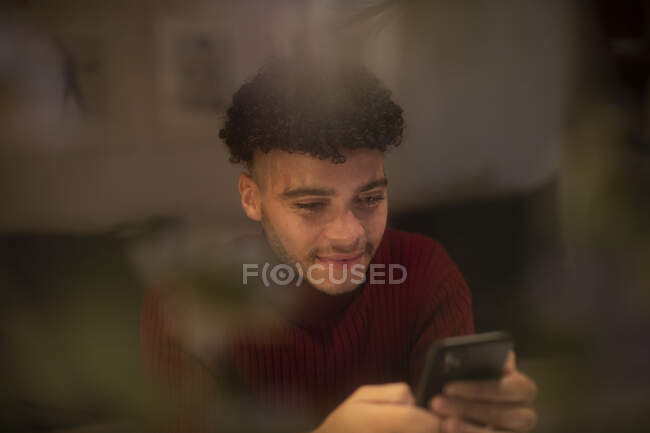 Sorridente giovane uomo utilizzando smart phone in finestra — Foto stock