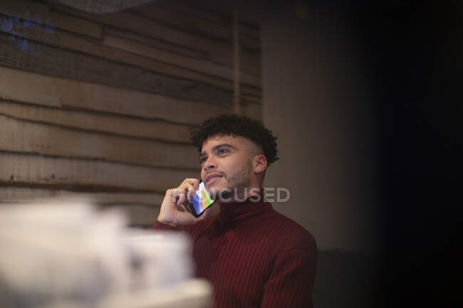 Young man talking on smart phone in home office — Stock Photo