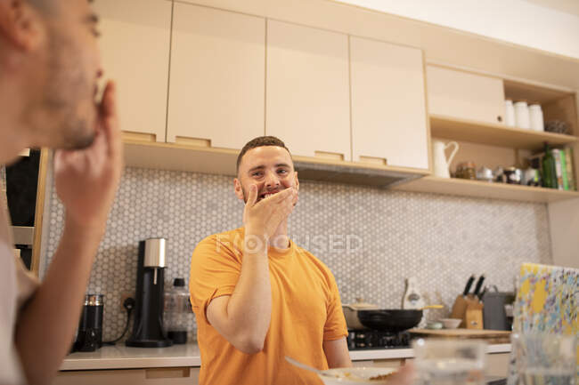 Feliz gay macho pareja riendo y comer en cocina - foto de stock