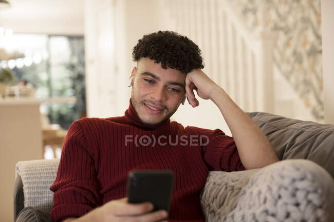 Young man using smart phone on living room sofa — Stock Photo