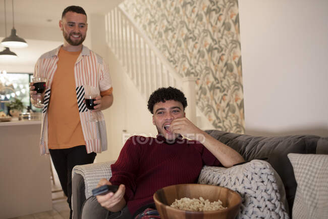 Feliz gay masculino casal com tinto vinho e pipoca assistindo TV no casa — Fotografia de Stock