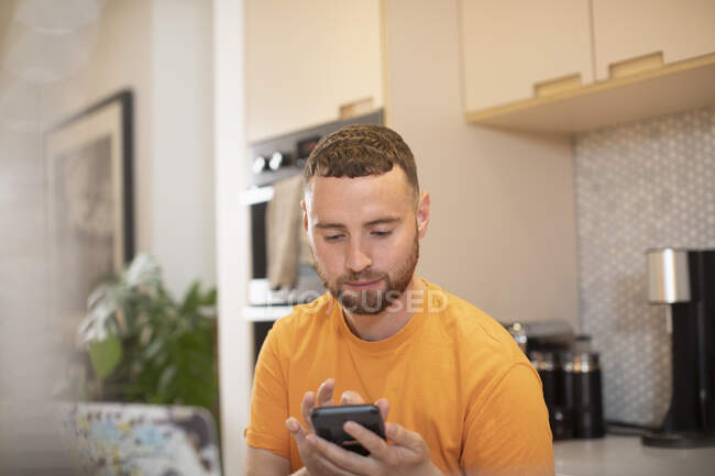 Молодой человек использует смартфон на кухне — стоковое фото