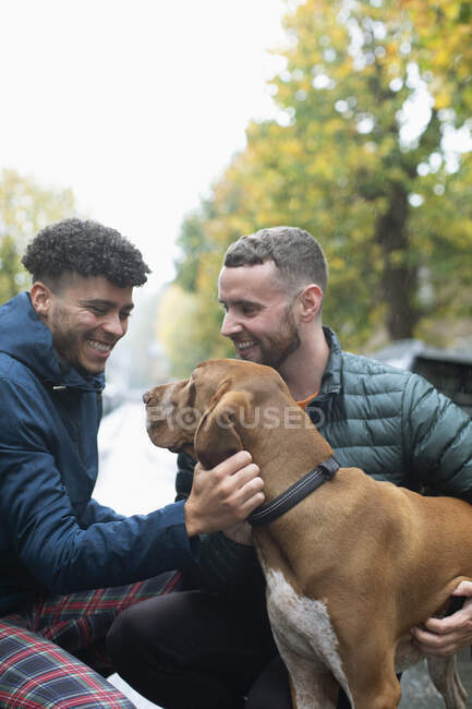 Happy gay male couple petting dog on street — Stock Photo
