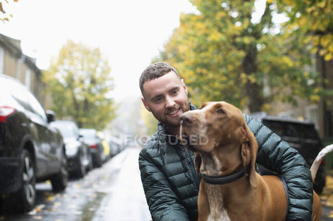 Felice giovane uomo con cane sulla strada urbana bagnata — Foto stock