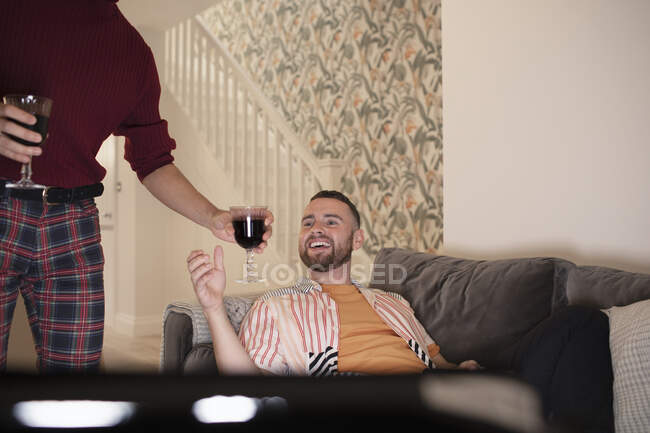 Feliz gay macho pareja disfrutando tinto vino y viendo televisión en casa - foto de stock