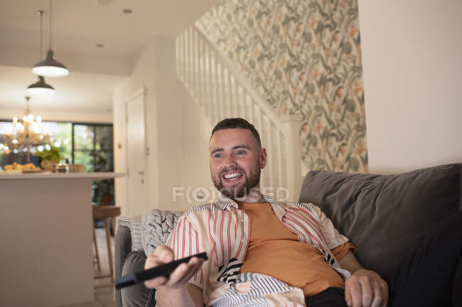 Joyeux jeune homme avec télécommande regardant la télévision sur le canapé — Photo de stock