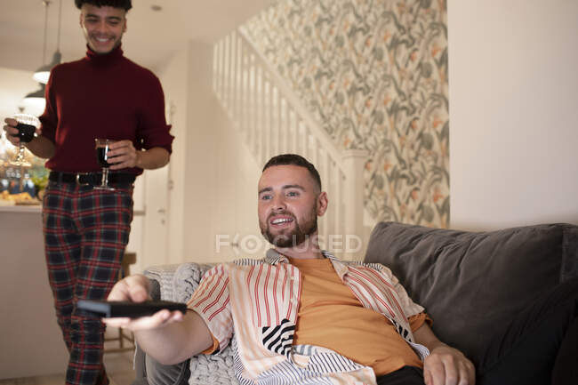 Gay macho pareja con vino viendo televisión en casa - foto de stock