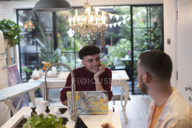 Gay male couple talking and using laptop in kitchen — Stock Photo