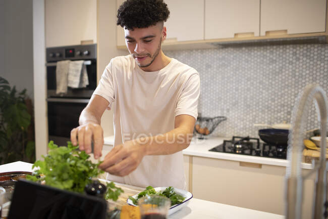 Young man cooking with fresh cilantro in kitchen — Stock Photo