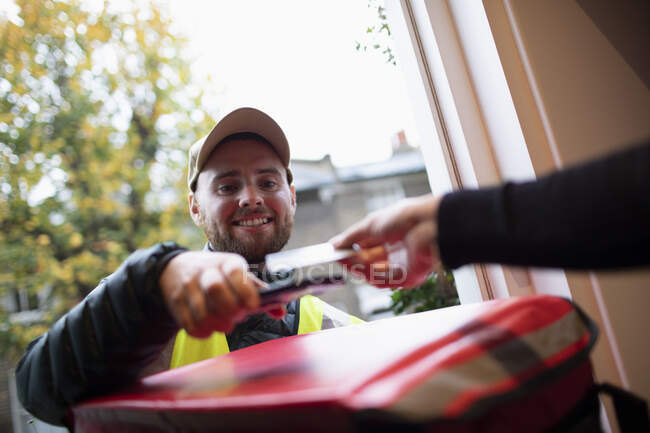 Man paying delivery man for food delivery with smart card at front door — Stock Photo