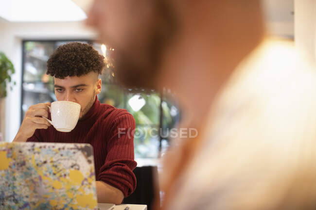 Молодий чоловік п'є каву, працюючи з дому на ноутбуці — стокове фото