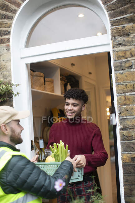 Hombre recibiendo la entrega de comestibles del repartidor en la puerta principal - foto de stock