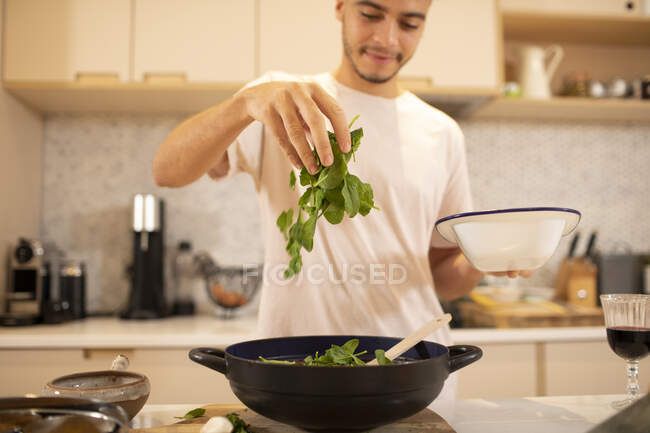Joven cocinando con espinacas frescas en la cocina - foto de stock