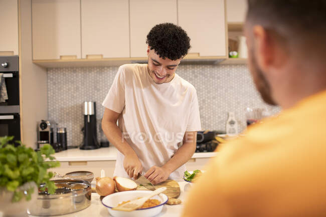 Jovem cozinhando cebola de corte na cozinha — Fotografia de Stock