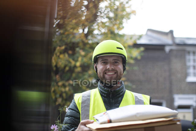 Retrato amigável homem de entrega no capacete entregando pacotes na porta — Fotografia de Stock